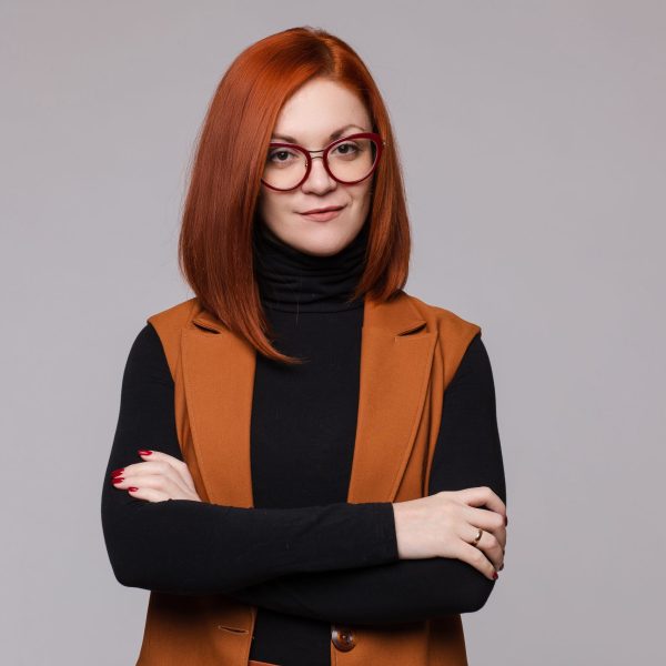 Portrait of smiling red-haired business woman in glasses posing looking at camera medium shot. Beauty European female boss standing with crossed hand isolated at white studio background